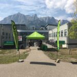 a green tent in front of a building. Bikes are parked in rows beyond the tent. Two community cruisers flags flank a path that leads to the tent