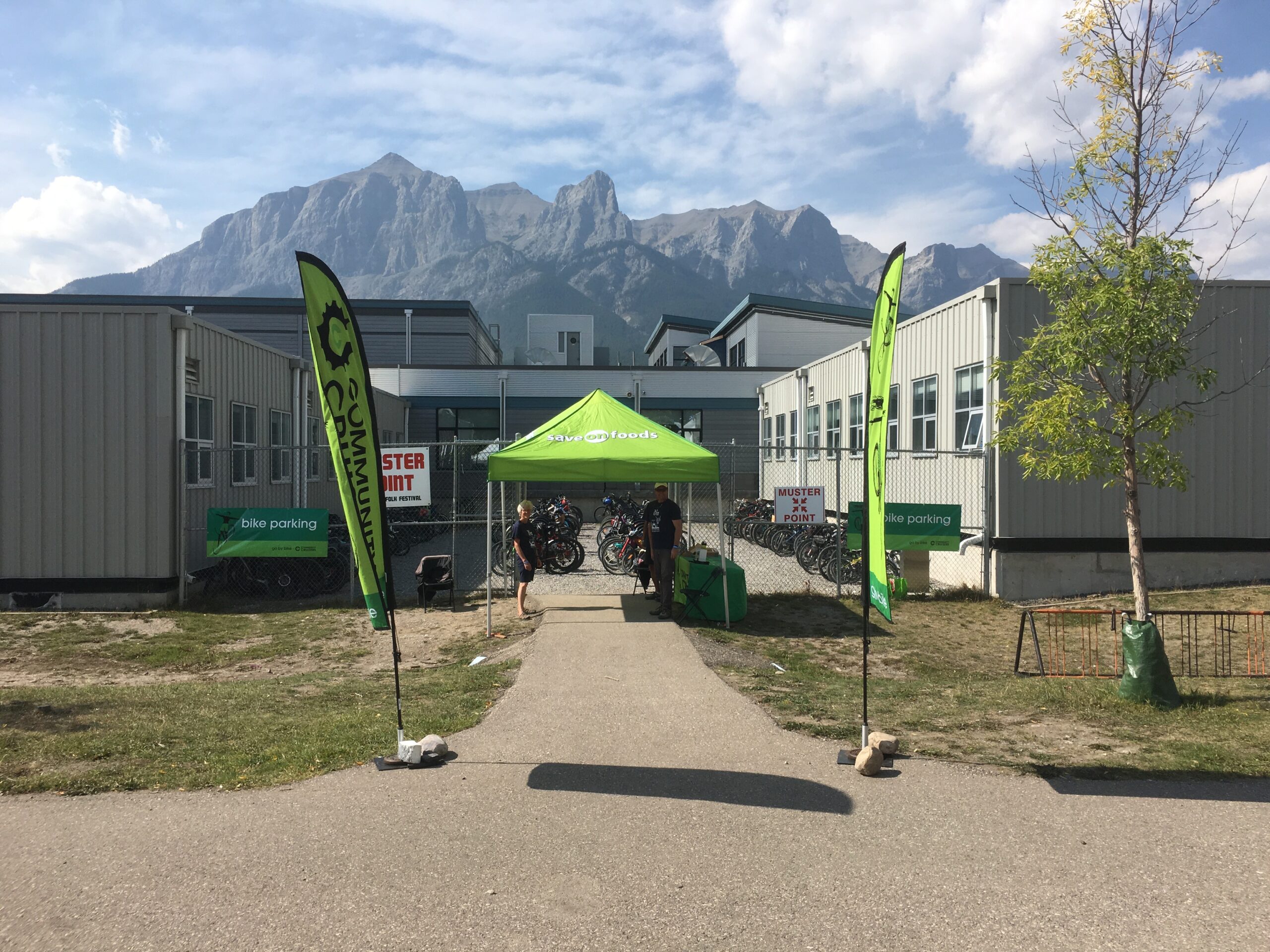 a green tent in front of a building. Bikes are parked in rows beyond the tent. Two community cruisers flags flank a path that leads to the tent